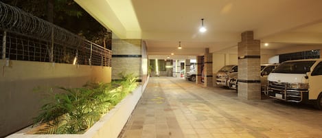 A parking area with a tiled floor, a white van, and a security fence.