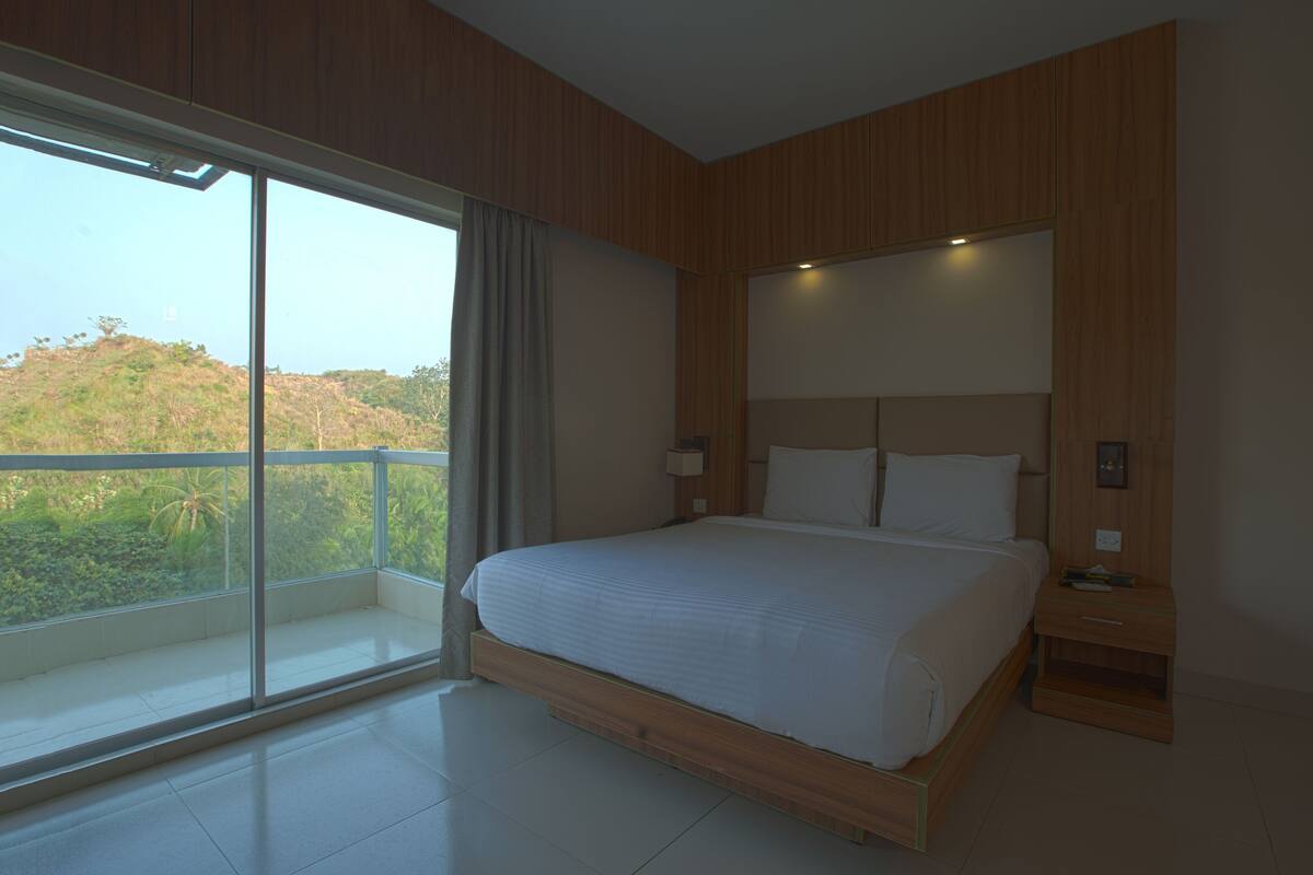 Un dormitorio moderno con una cama grande, una mesita de noche y vistas a zonas verdes a través de una puerta corredera de vidrio.