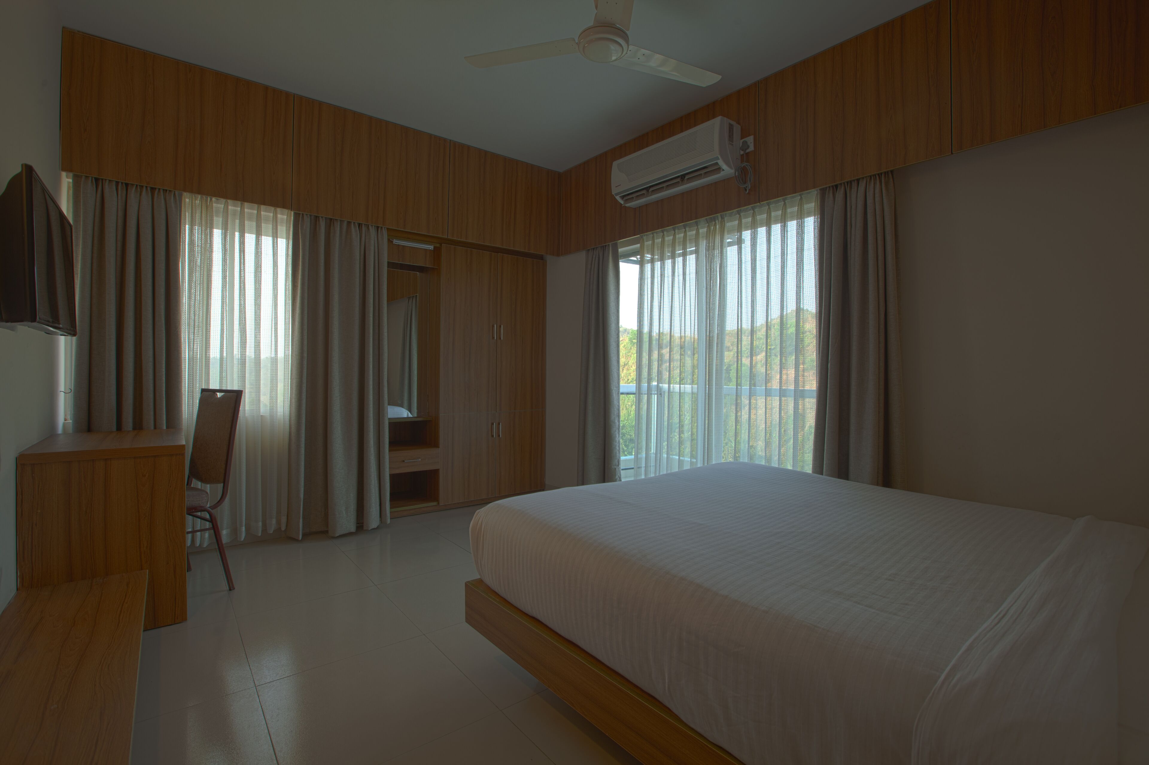 Ein Hotelzimmer mit einem großen Bett, einem Schreibtisch und einem Stuhl. Es gibt einen Deckenventilator und eine Klimaanlage.