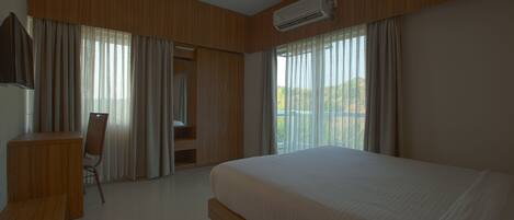 Ein Hotelzimmer mit einem großen Bett, einem Schreibtisch und einem Stuhl. Es gibt einen Deckenventilator und eine Klimaanlage.
