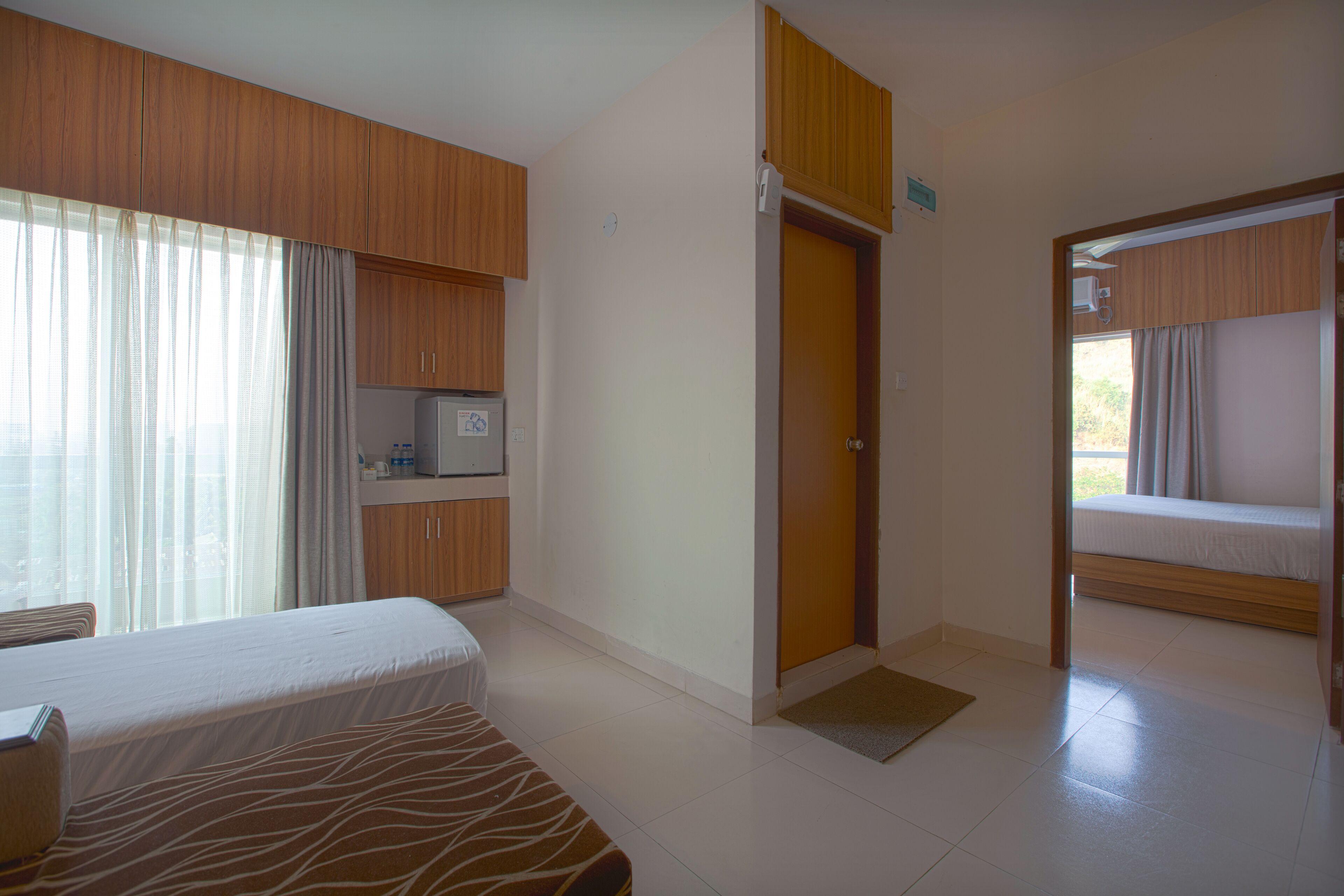 A hotel room with a bed, a desk, a wardrobe, a microwave, and a door leading to another room.