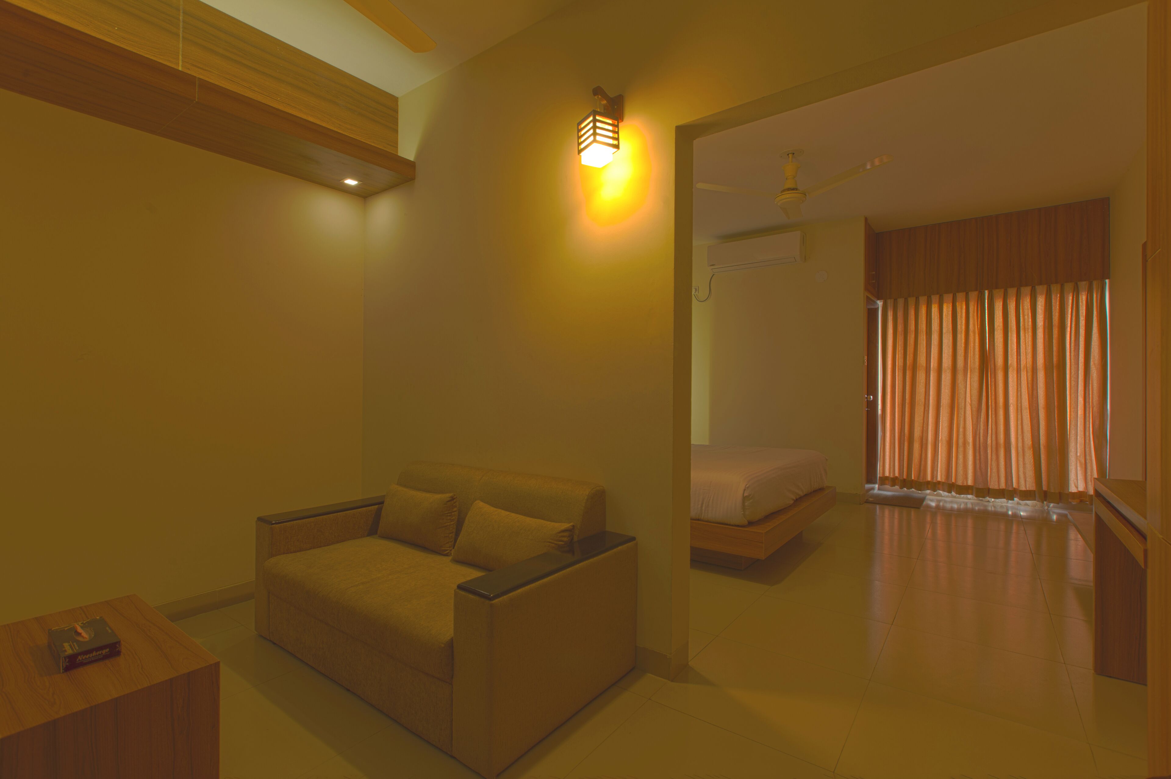 A hotel room with a sofa, a bed, a ceiling fan, and a wall-mounted light fixture.
