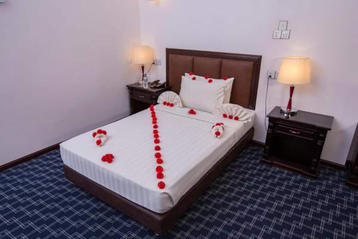 A neatly made bed with a white bedspread and red flowers, two bedside tables with lamps, and a blue patterned carpet.