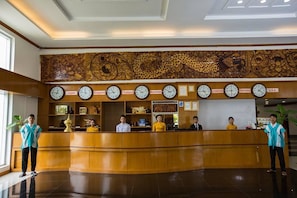 A hotel reception area with a wooden reception desk, multiple clocks displaying time in various countries, and a decorative wall above.