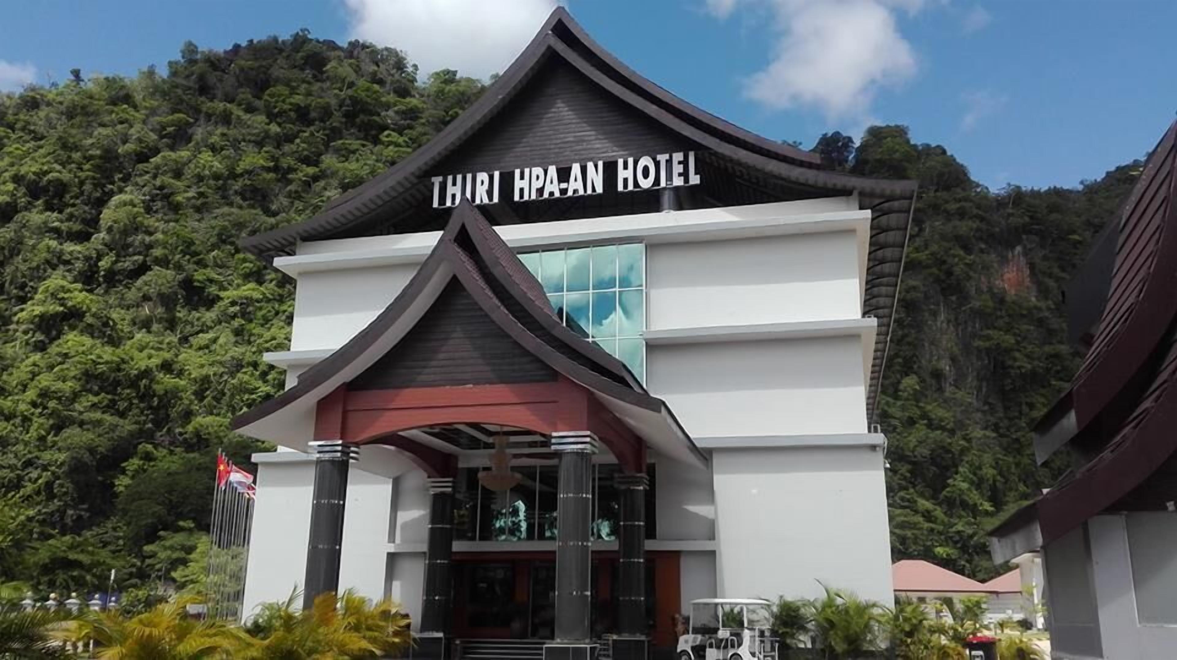 The Thiri Hpa-An Hotel with a modern architectural design, featuring a prominent entrance and a view of the surrounding lush greenery.