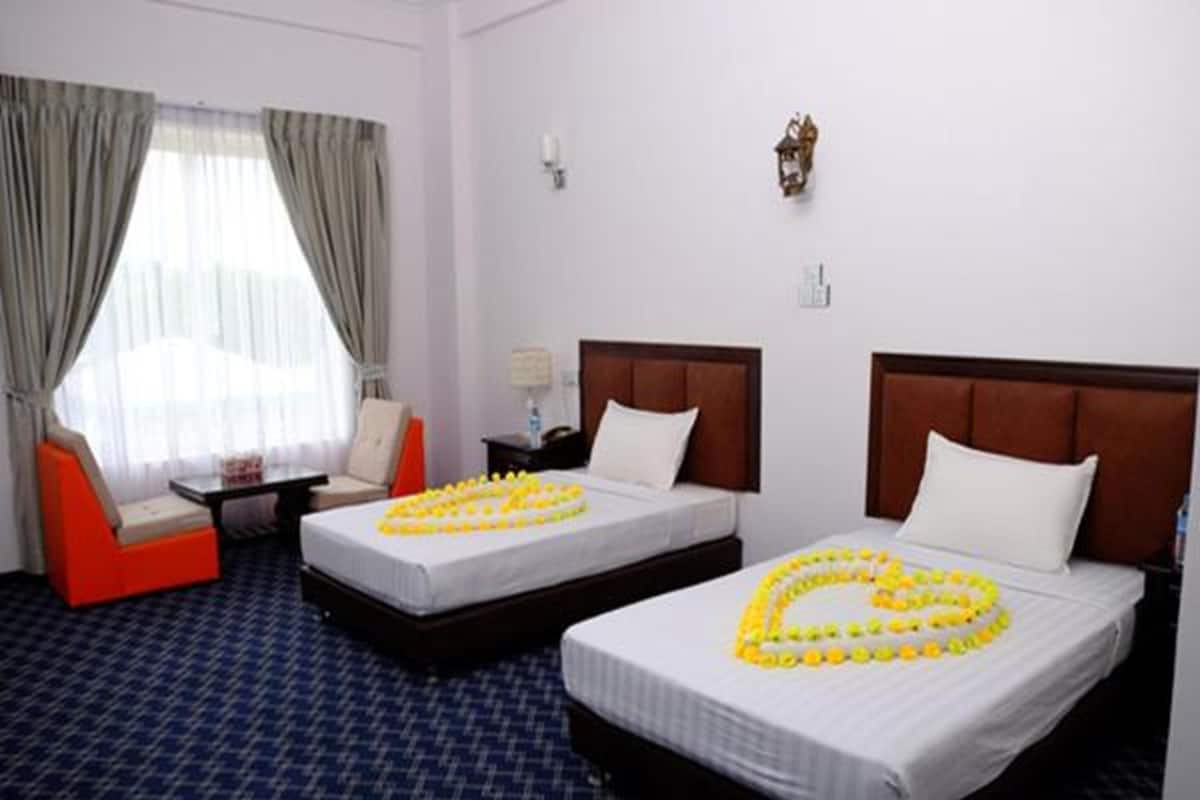 A hotel room with two beds, a small table, a chair, and a window with curtains.