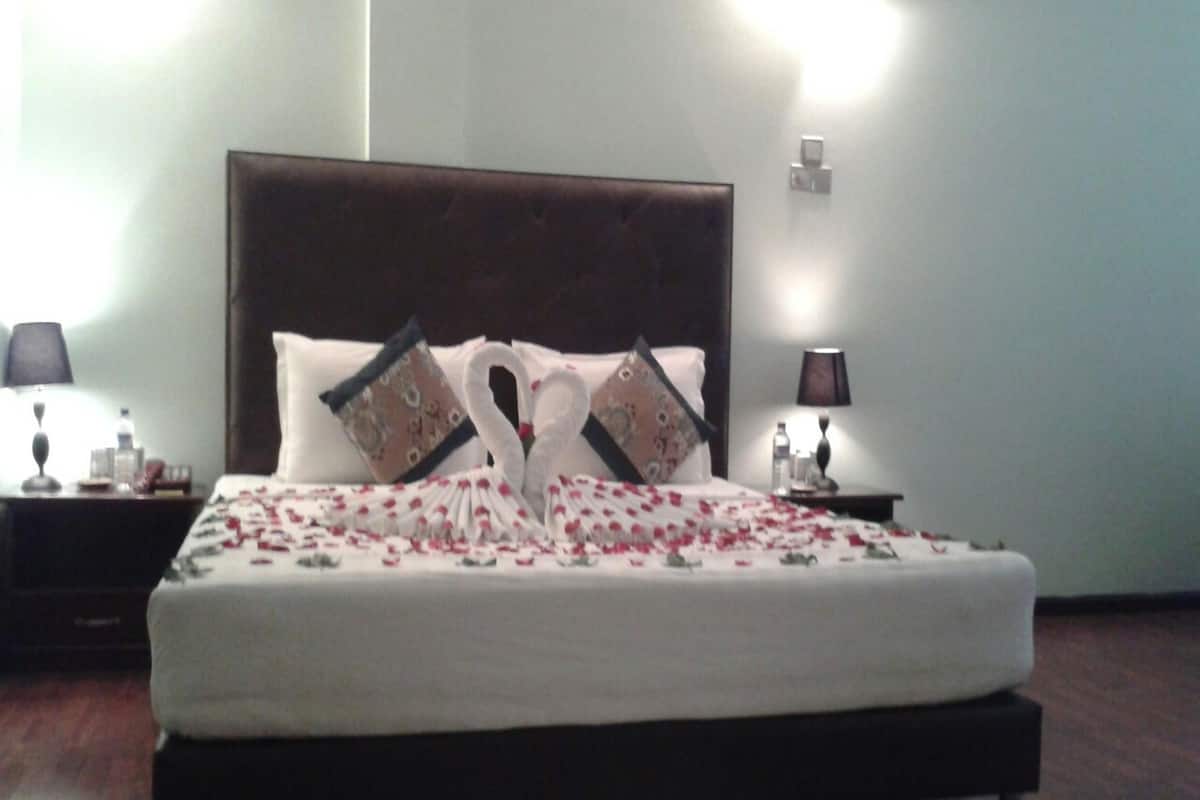 A neatly made bed with a decorative swan pillow arrangement, a dark headboard, and bedside lamps.