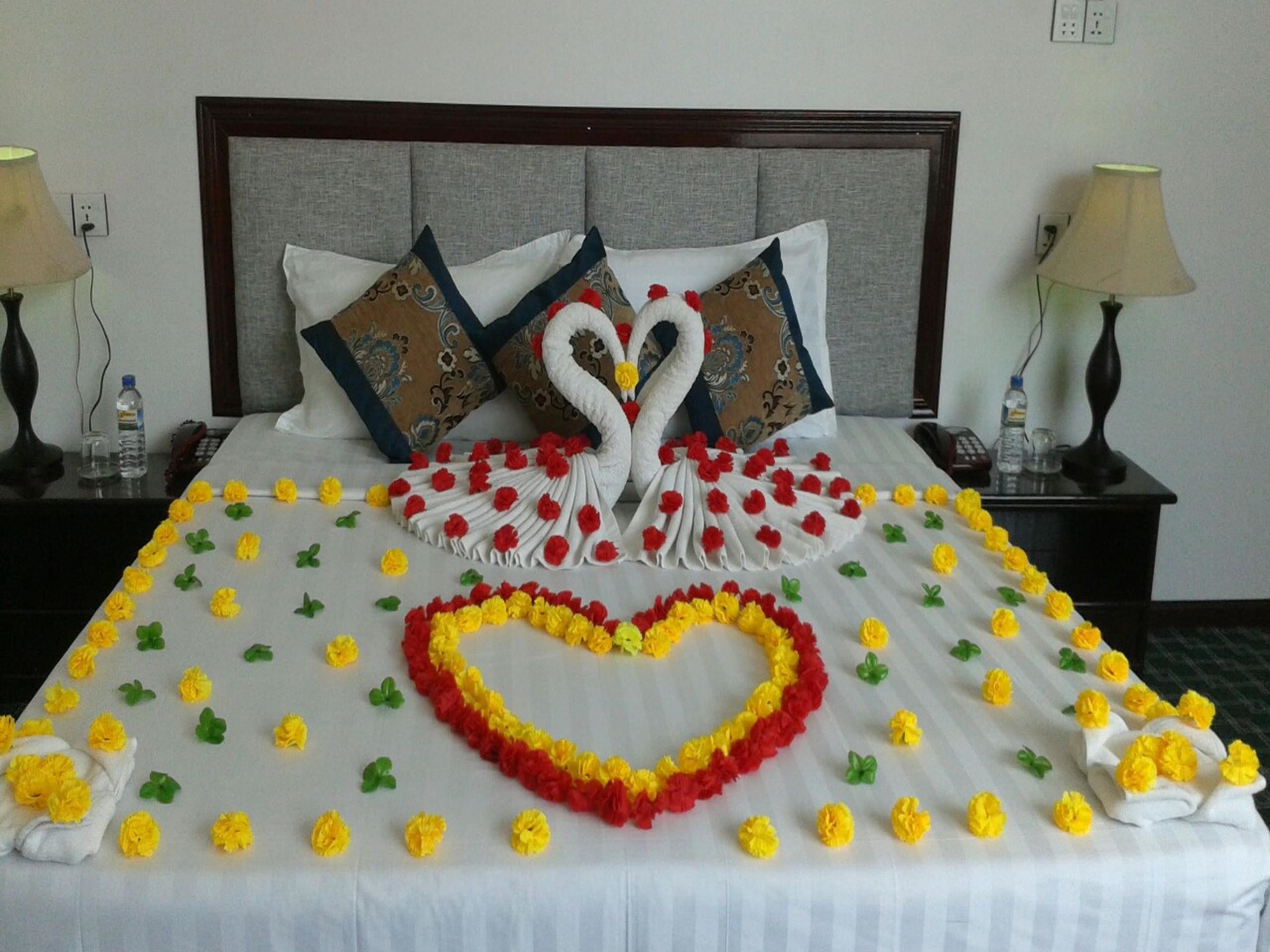 A neatly made bed with a swan and heart design, pillows, and a floral arrangement.