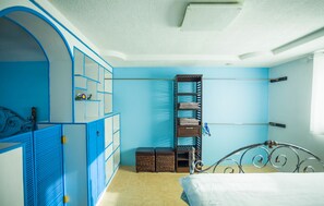 A bedroom with a bed, a wardrobe with blue doors, a metal bed frame, and a shelf unit against the wall. - Joy House (Saipan)