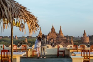 A terrace with wooden chairs and tables, overlooking ancient temple structures.