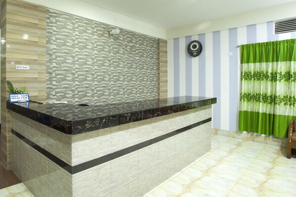 A reception area with a marble counter, a patterned wall, a clock, and a green curtain.