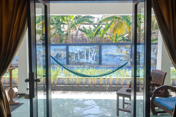 Una puerta de vidrio da a un patio con una hamaca, sillas de madera y un mural de una cascada.