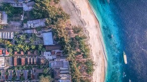 Vista aérea de una zona costera con edificios, una playa de arena y aguas azules cristalinas.