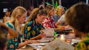 Een groep mensen zit aan een tafel met menukaarten, kaarsen en een fles.