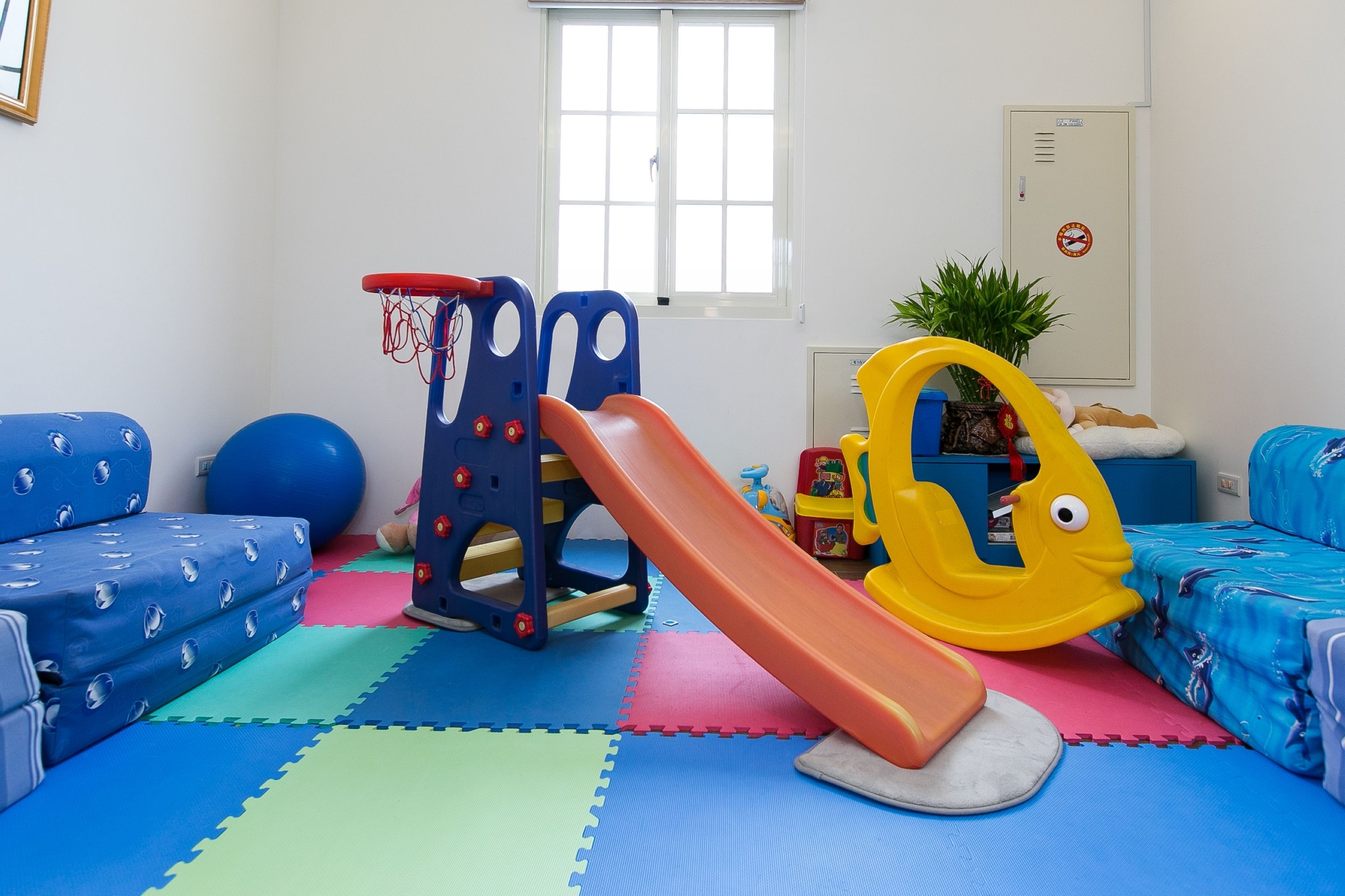 Une salle de jeux avec un toboggan, des tapis en mousse bleus et roses, et un canapé bleu.