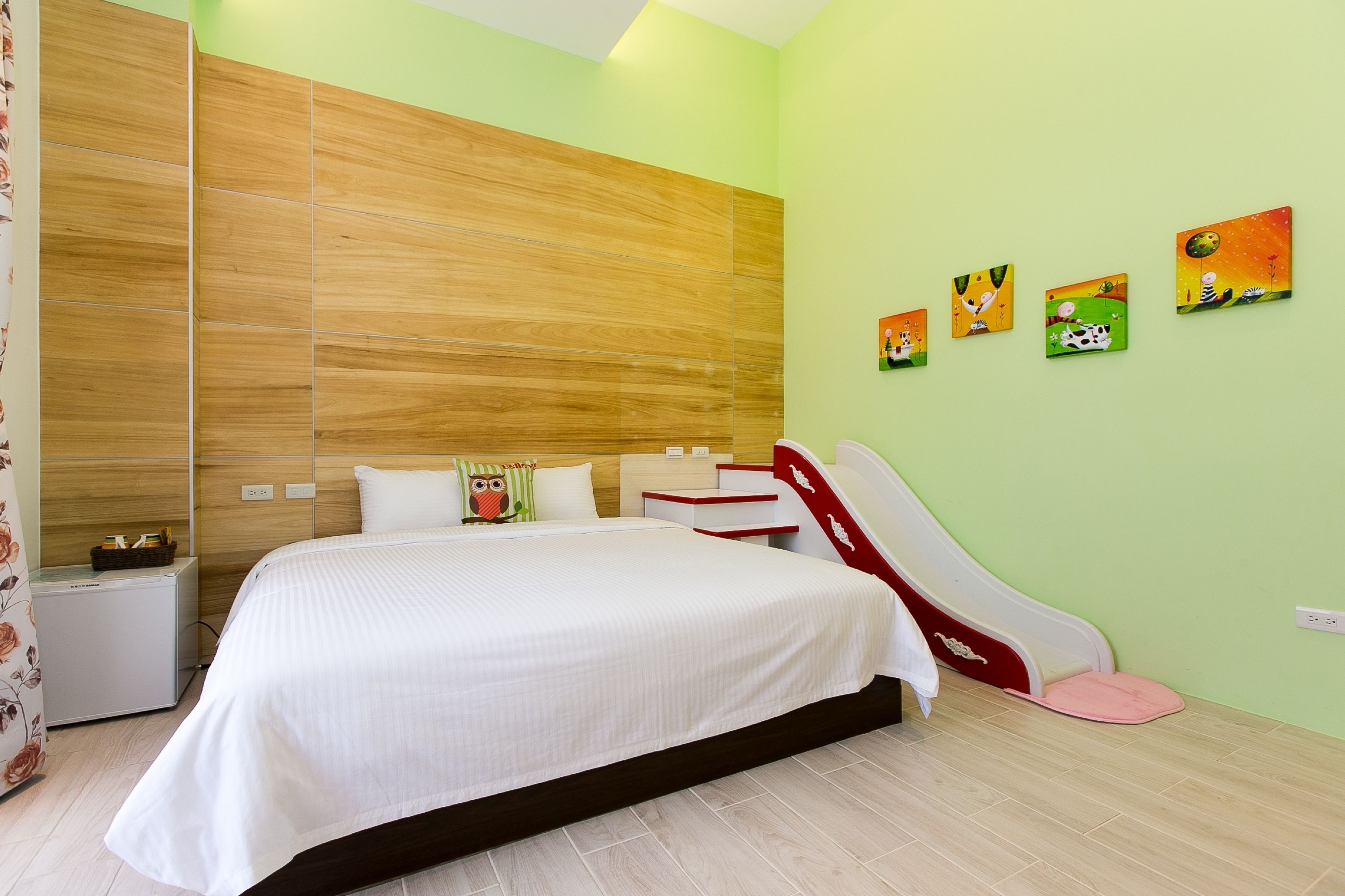 A modern bedroom with a large bed, a wooden headboard, a small bedside table, a nightstand, and a wall-mounted shelf.