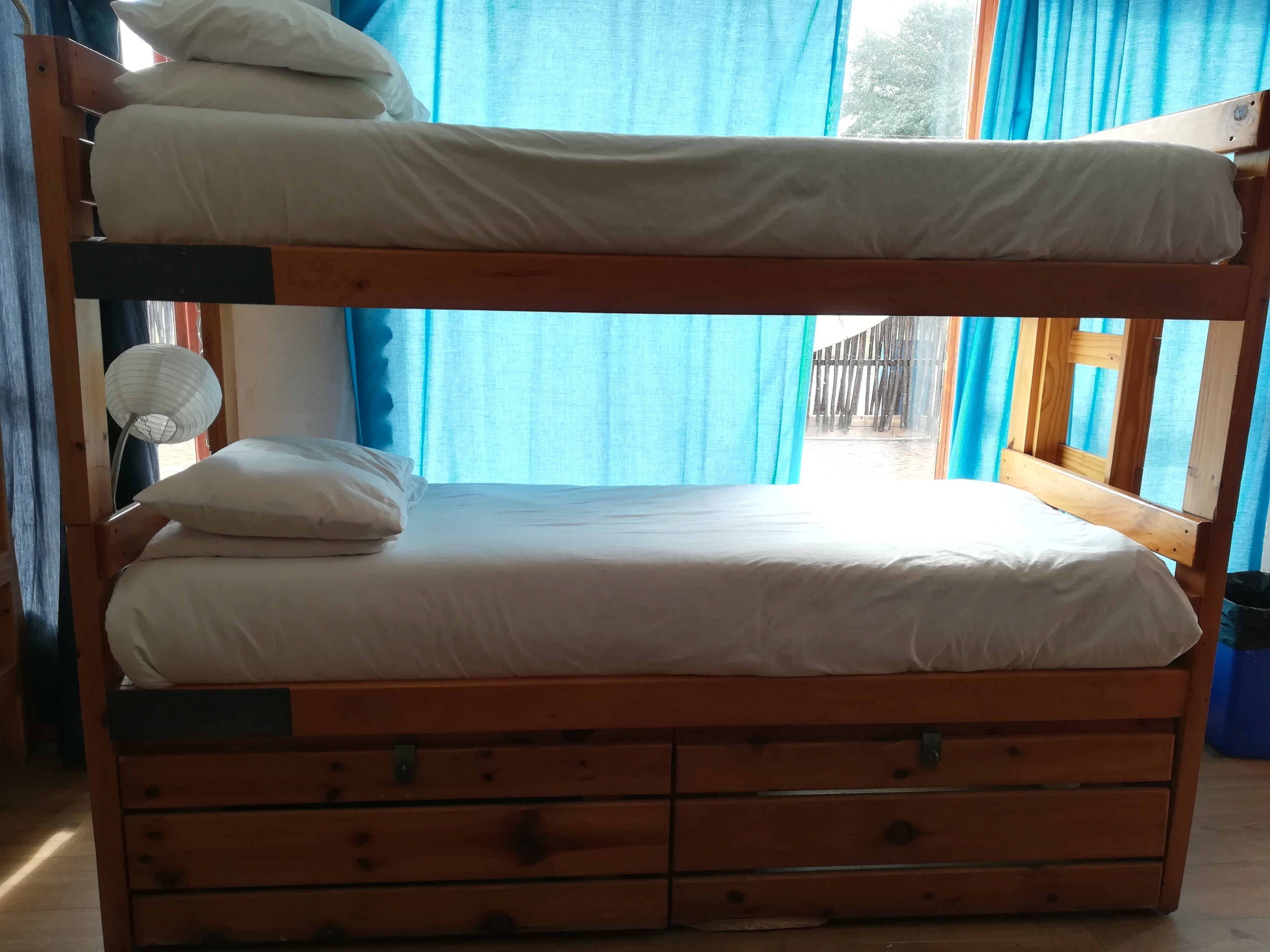 Una cama litera con estructura de madera, ropa de cama blanca y un pequeño ventilador.