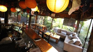 A bar area with wooden furniture, hanging paper lanterns, and a view of greenery outside. - Saltycrax Backpackers and Adventures (Cape Town)
