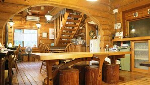 A rustic wooden interior with a dining table, chairs, a staircase, and a kitchen area. - Canadian Loghouse Inn Azumino Yujin (Azumino)