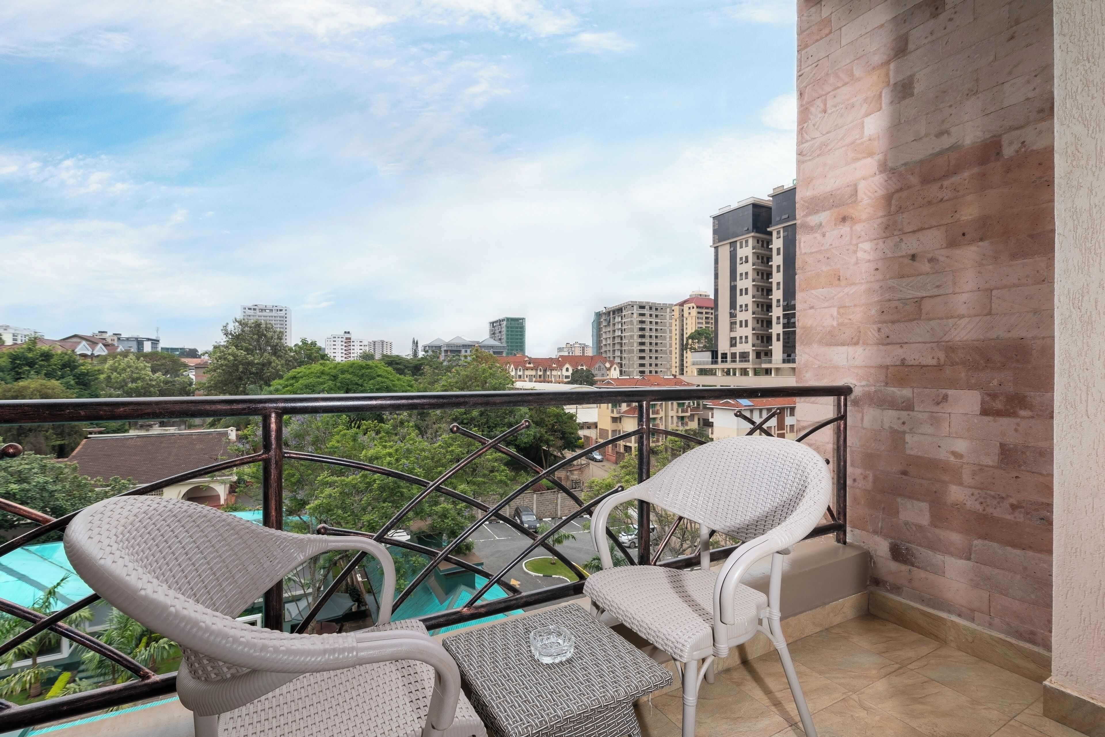 Un balcon agrémenté de fauteuils en osier et d’une petite table, offrant une vue sur une piscine et le paysage urbain.