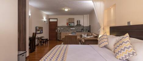 Un dormitorio con una cama grande, un escritorio y una kitchenette al fondo.