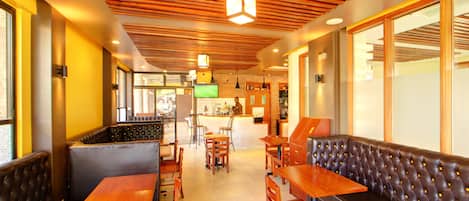 A restaurant interior with wooden tables and booths, a counter with a TV, and a tiled floor.