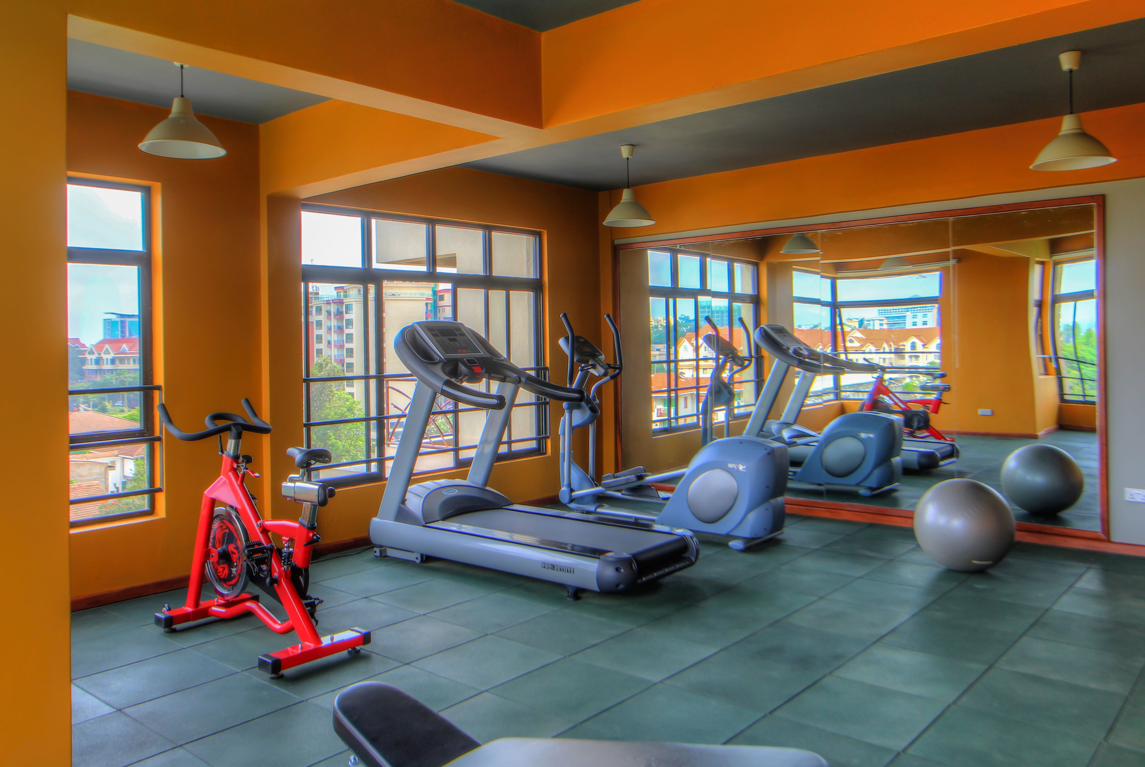 A gym with exercise equipment, large windows, and a view of buildings outside.