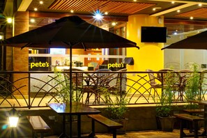 Un área de estar al aire libre con mesas y sombrillas, una barra con un letrero que dice "pete's", y un televisor montado en la pared.