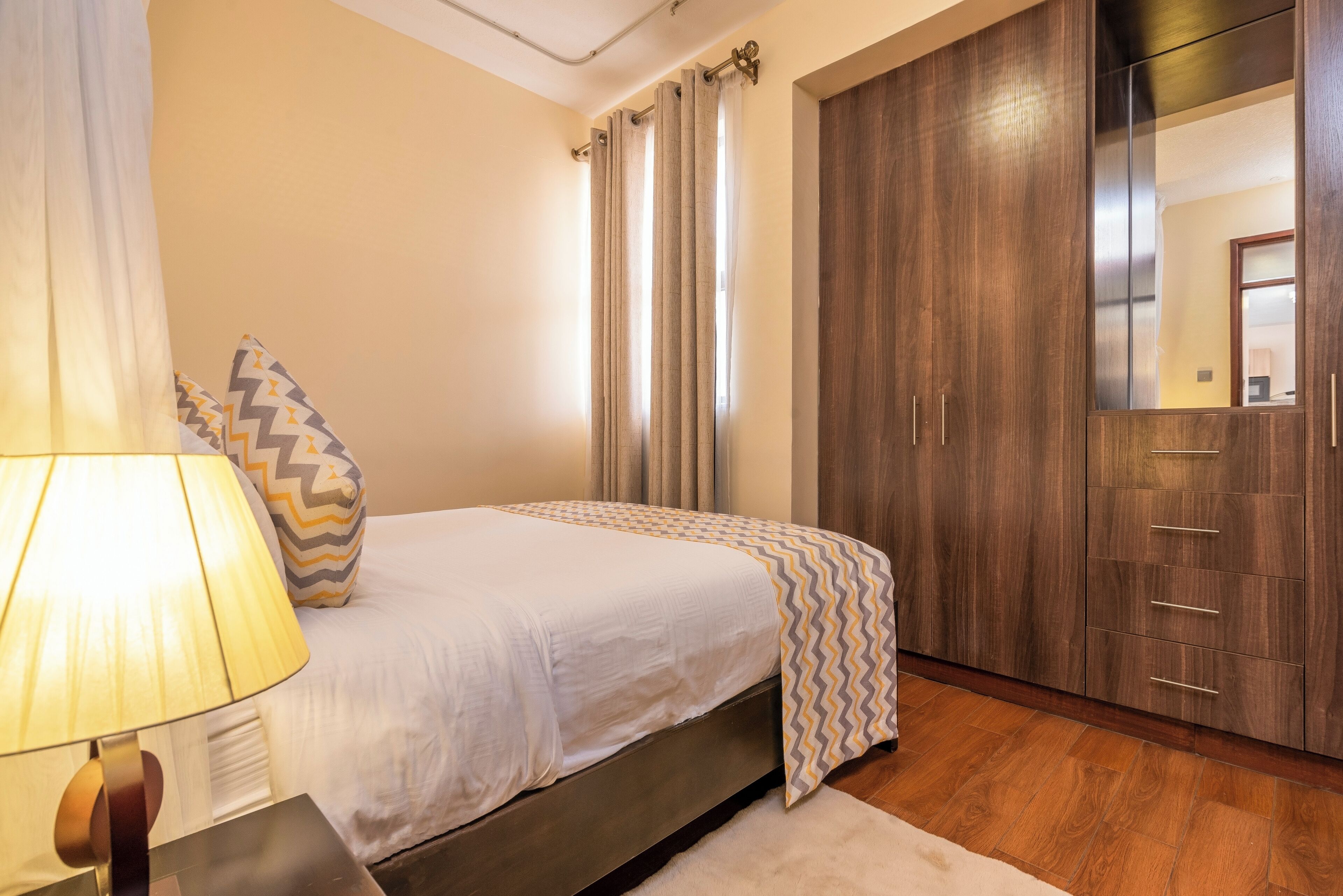 A bedroom with a bed, a nightstand, a lamp, a wardrobe, and a mirror.