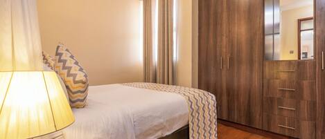 A bedroom with a bed, a nightstand, a lamp, a wardrobe, and a mirror.