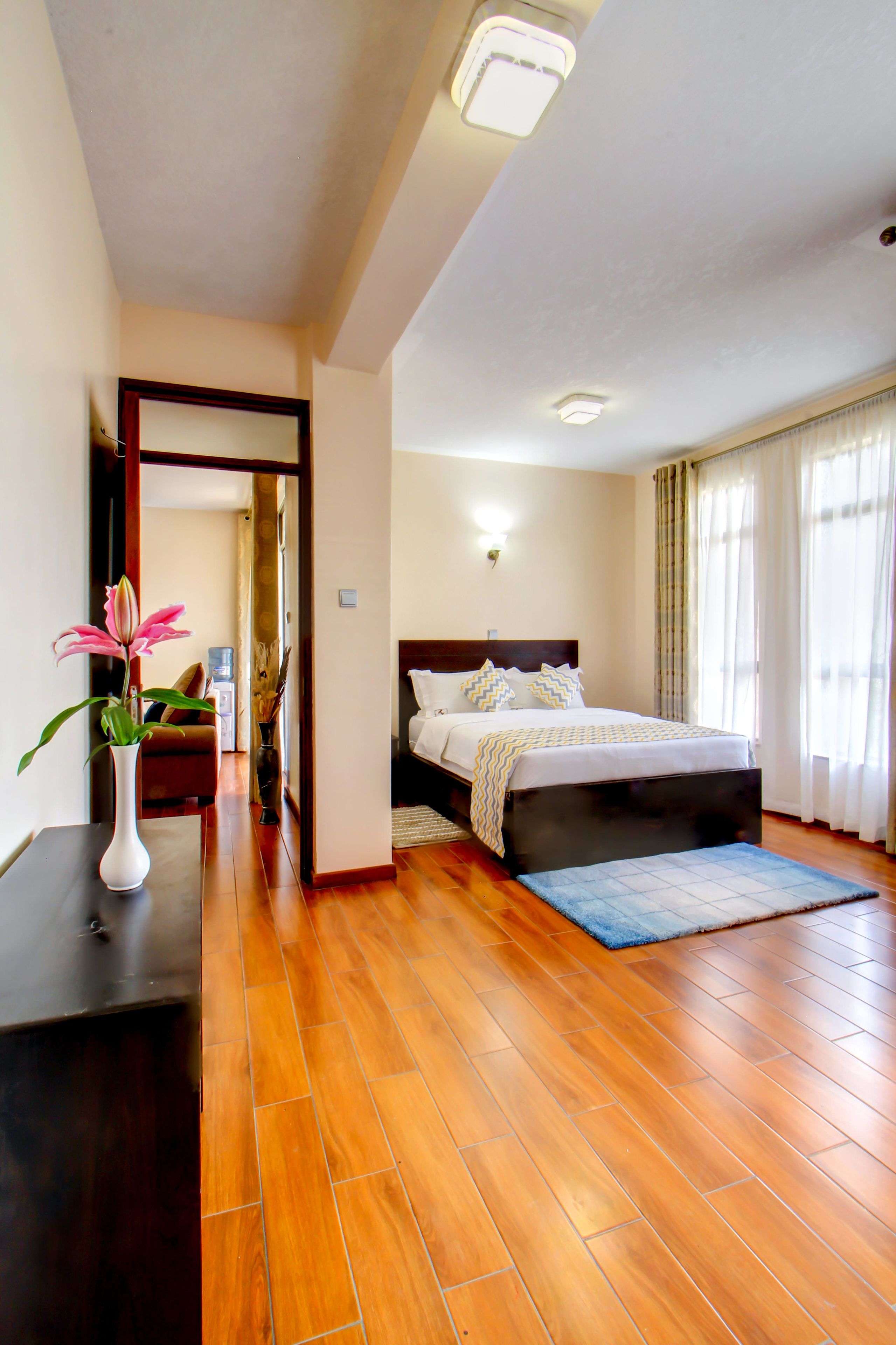 Un dormitorio con suelo de madera, una cama con cabecera, una mesita de noche y un jarrón con flores.