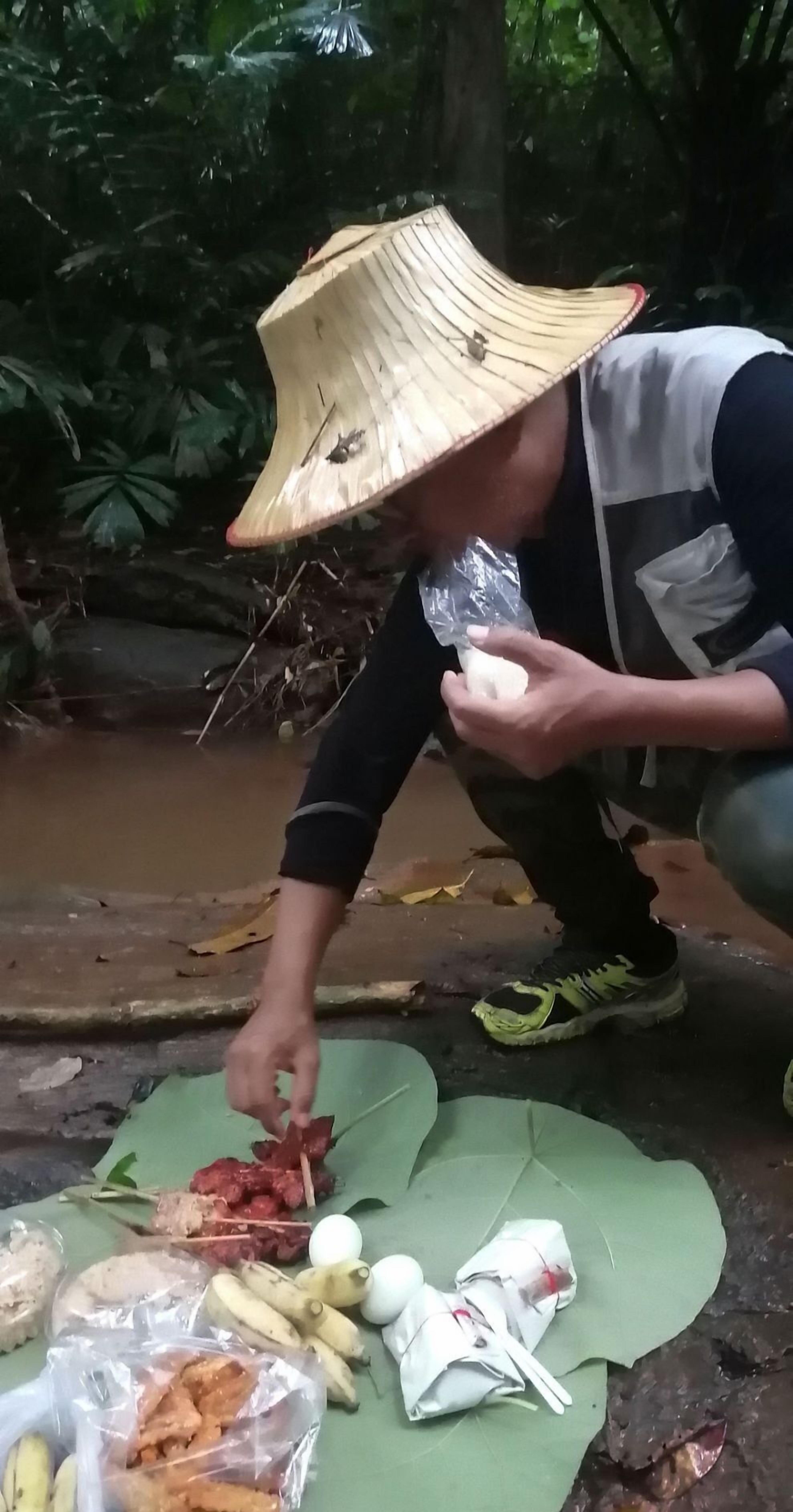 Una persona con sombrero preparando comida al aire libre, con diversos objetos sobre una esterilla.
