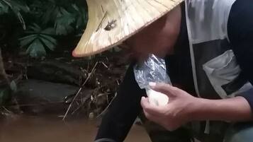 Una persona con sombrero preparando comida al aire libre, con diversos objetos sobre una esterilla.