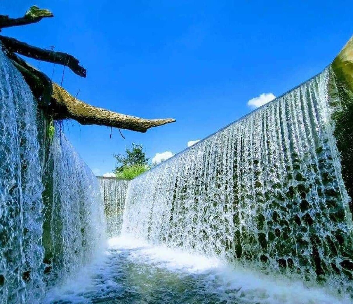 A waterfall cascading down a narrow, rocky channel with a clear blue sky above.
