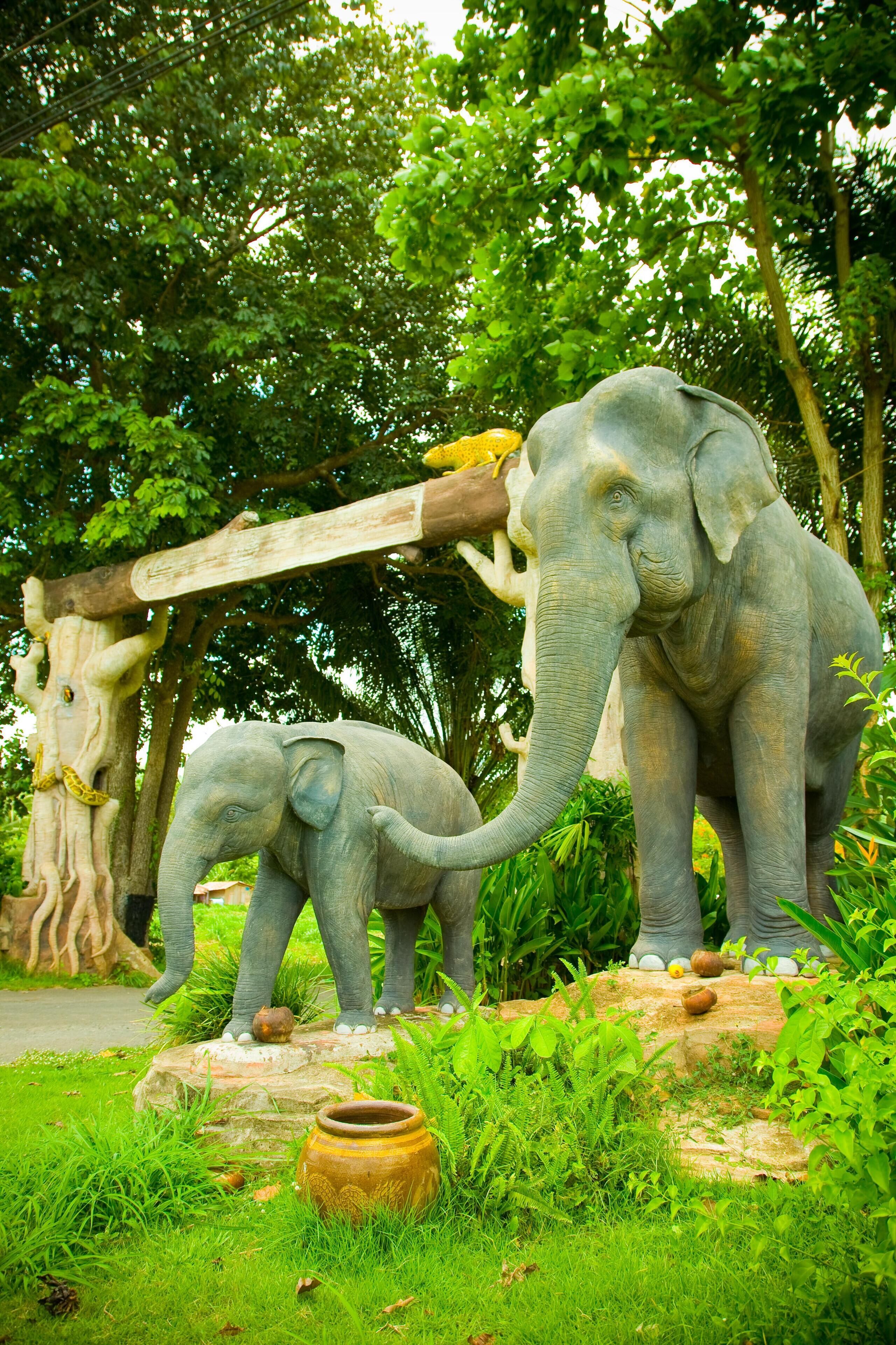 Une sculpture représentant deux éléphants sur un rocher, avec un tronc d’arbre et une poutre en bois en arrière-plan.