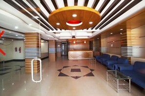 Een moderne hotel lobby met een receptiebalie, een blauwe zithoek en een geometrisch vloerpatroon.