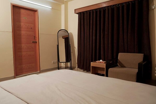 Een hotelkamer met een bed, een stoel, een klein tafeltje met zakdoekjes en een spiegel, plus een deur.