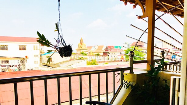 A balcony with a view of a temple and buildings. There is a chair and a table on the balcony. - Fancy Guest House (Phnom Penh)