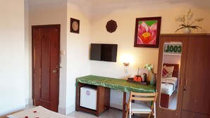 A hotel room with a bed, a desk with a chair, a television, a small refrigerator, and a wardrobe. - Fancy Guest House (Phnom Penh)