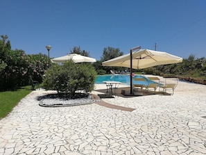 A pool area with tiled flooring, outdoor seating, and umbrellas. - Agriturismo I Mandorli (Triei)