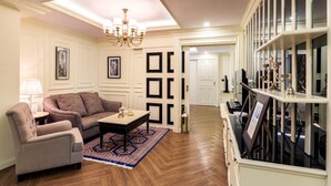 A living room with a sofa, armchair, and coffee table, a chandelier, and a bookshelf with decorative items. - LA49 Hotel (Bangkok)
