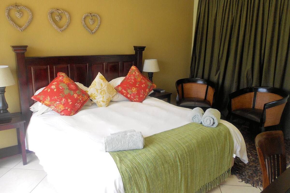 A hotel room with a bed, pillows, a green throw blanket, a chair, a lamp, and heart-shaped wall decorations.