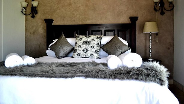 Una cama con cabecera de madera, varias almohadas, un edredón mullido y lámparas fijadas a la pared.