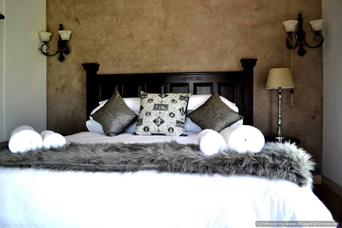 A bed with a wooden headboard, multiple pillows, a fluffy blanket, and wall-mounted lamps.