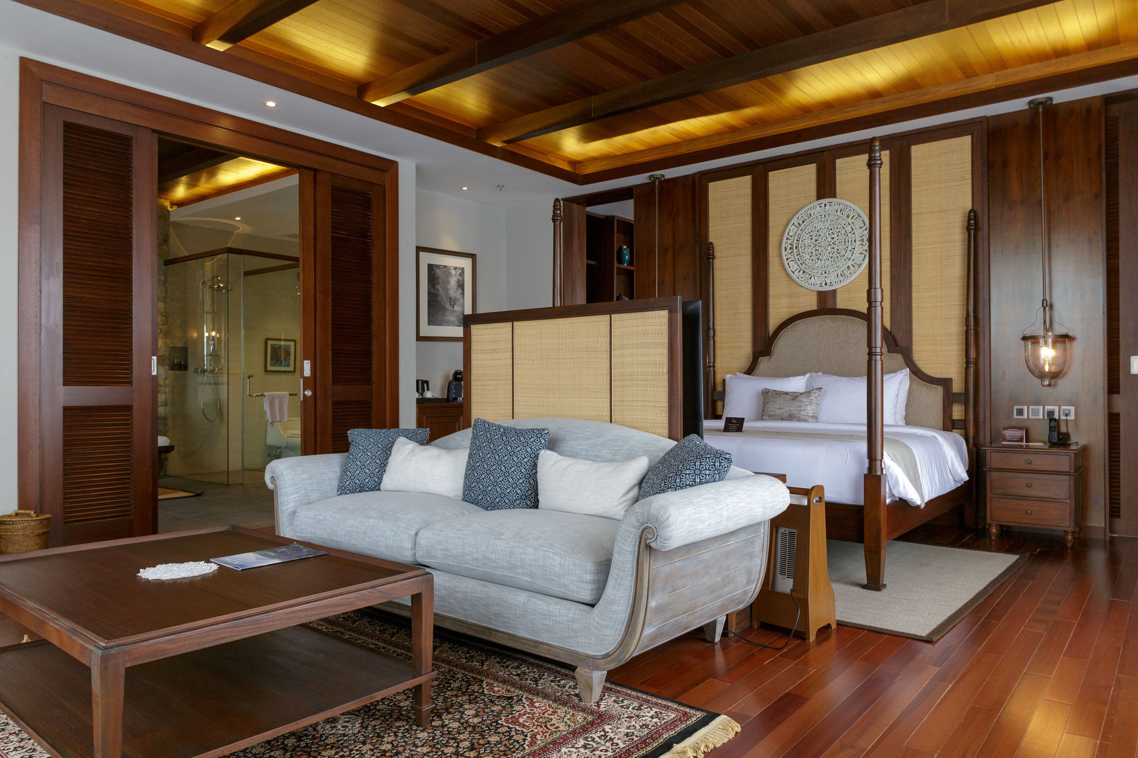 A modern hotel room with a wooden ceiling, a sofa, a bed, a bedside table, and a nightstand.