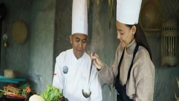 A chef and a server in a kitchen with pots, vegetables, and cooking utensils.