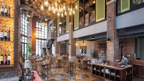 A spacious restaurant with high ceilings, hanging light fixtures, and a brick wall with wine bottles. - Plataran Bromo (Wonokitri)