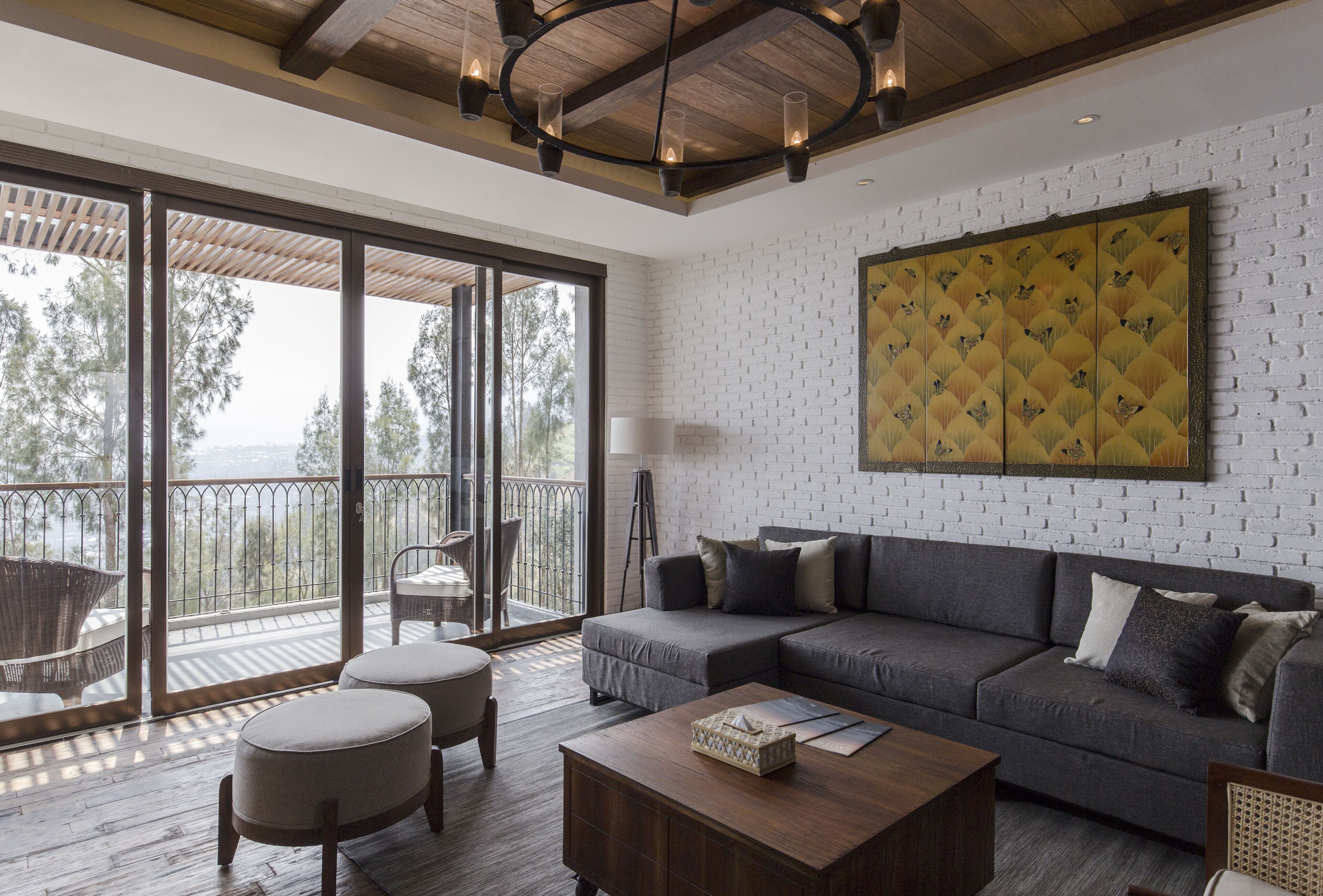 A modern living room with a grey sectional sofa, ottomans, a wooden coffee table, and a large window overlooking a balcony.