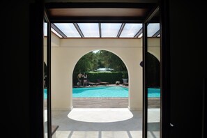 Una piscina interior con techo de cristal, rodeada de sillones de descanso y setos.