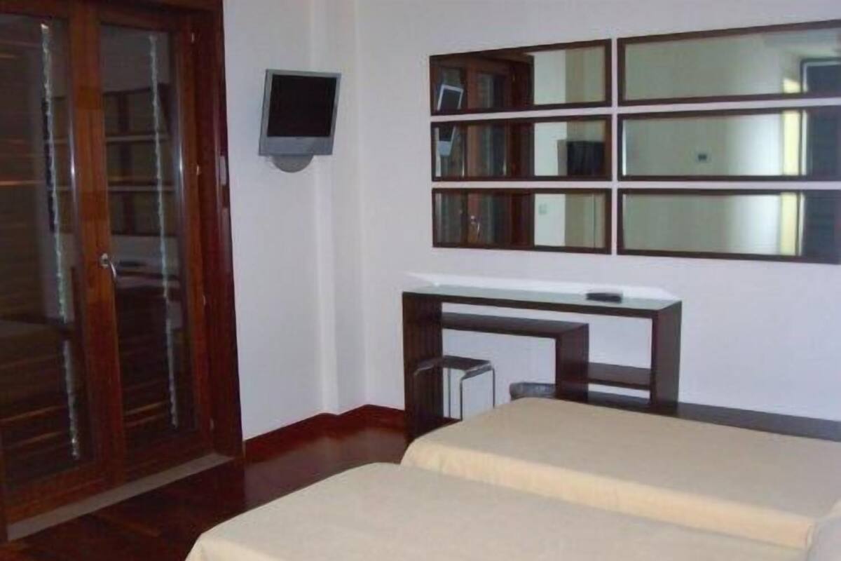A room with a bed, a desk, and a television mounted on the wall.